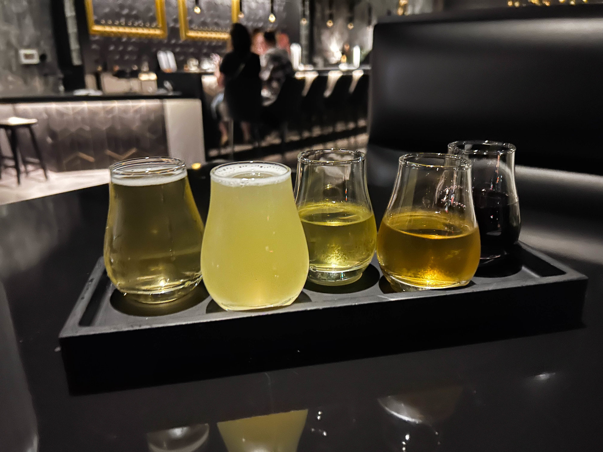 four glasses in a flight with mead on a black table
